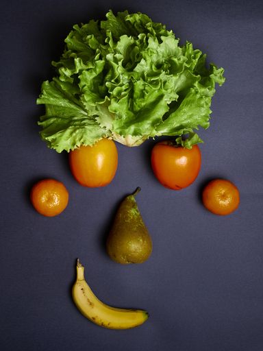 A vertical shot of a funny face made with fruits and lettuce