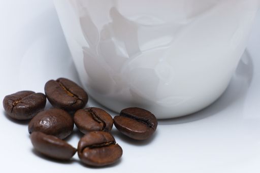A closeup of freshly roasted coffee beans on a saucer of a white ceramic cup