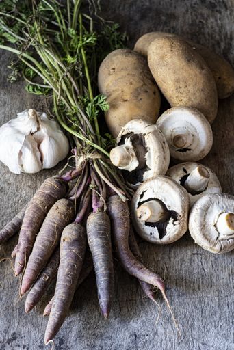 A vertical shot of garlic, potatoes, mushroom and carrots on a wooden surface