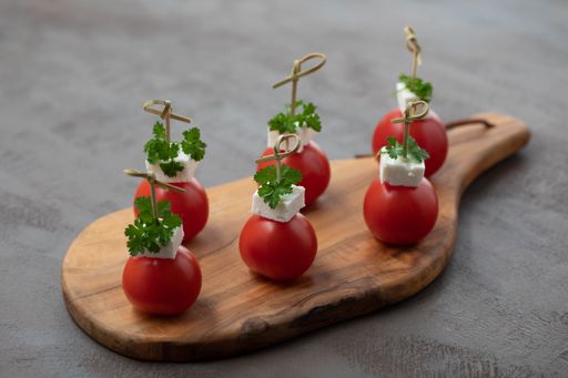 A closeup shot of tomatoes, feta cheese, and parsley on a wooden kitchen board.