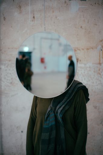 A vertical shot of a person standing behind a circular mirror