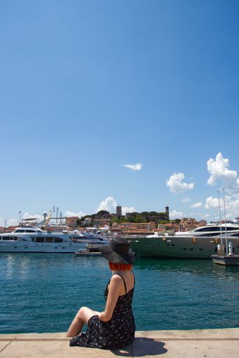 A vertical shot of a female sitting on the pier by the water captured in Cannes