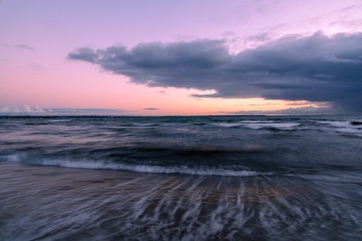 A breathtaking view of the wavy ocean gleaming under the cloudy pink sky - great for wallpapers