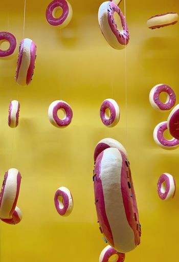 A vertical shot of donut figures hanging from ropes against a yellow background