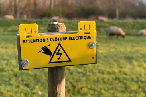 A selective focus shot of an "Electric fence" warning sign in French
