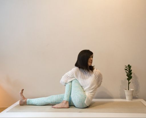 A horizontal shot of a young girl doing a yoga pose on the yoga mat with a flower pot at home
