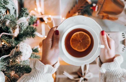 A top view of a female holding a cup of tea with lemon next to a Christmas tree