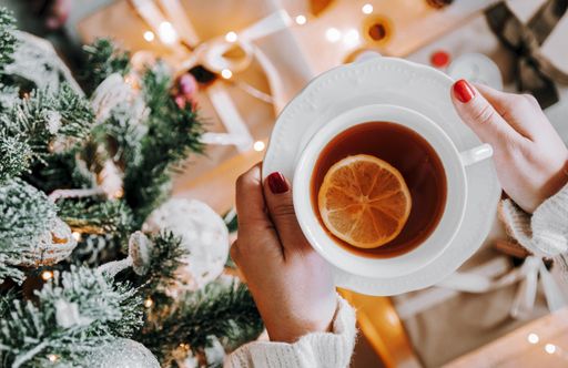 A top view of a female holding a cup of tea with lemon next to a Christmas tree