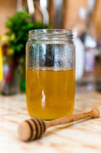 A Closeup shot of the honey in a jar with a honey dipper on the table