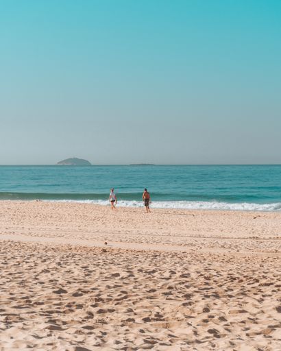 A beautiful view of a couple taking a walk on the sandy beach under the blue sky