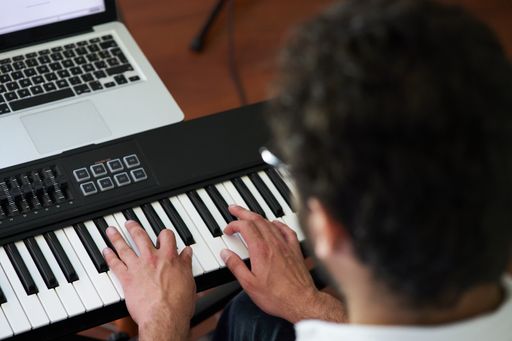 A high angle back view of male musician hands playing on electronic piano keyboard in a studio