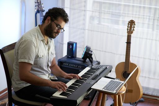 A talented concentrated Hispanic male musician sitting and playing electronic piano in a studio