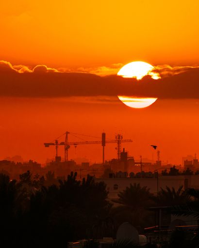 A vertical shot of the sun setting over the busy city, in the bright orange sky