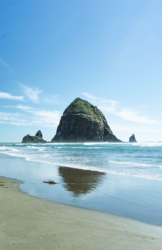 A vertical shot of sea waves washing the sandy beach with a massive rock in the background