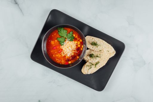 A high angle shot of a bowl of traditional soup and some bread on a plate
