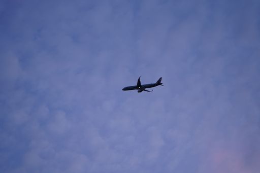 A low-angle shot of an airplane flying against the cloudy blue sky