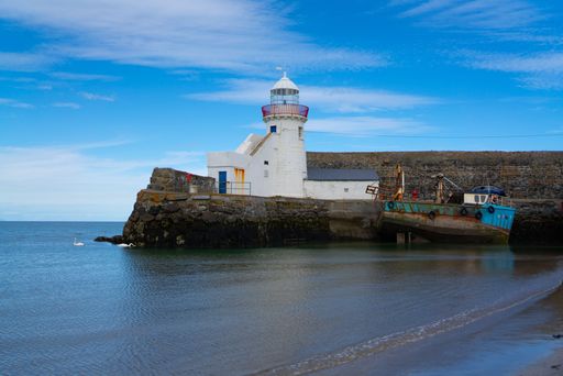 An idyllic scene featuring a small lighthouse perched on a rocky outcropping on the shoreline at low tide