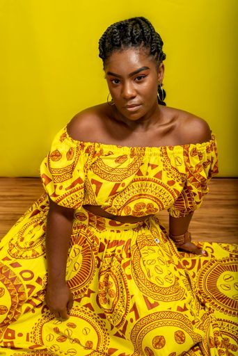 Young beautiful woman, serious, looking at the camera, sitting on a wooden floor. Against yellow background.