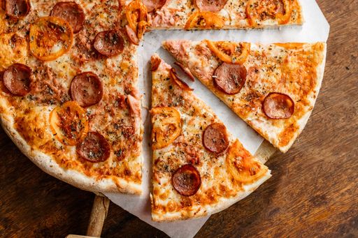 Top view of a freshly prepared pizza on a wooden cutting board, with a slice cut out