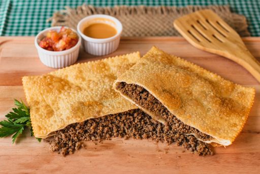 A closeup of a Brazilian pastry known as pastel, with a golden-brown crisp crust featuring a savory filling