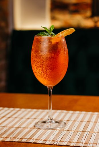 A colorful vertical shot of a delicious red alcoholic beverage garnished with an orange slice on the rim