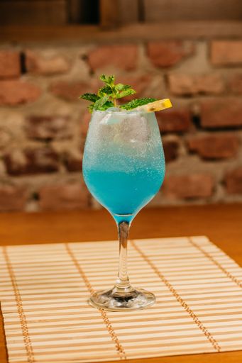 A refreshing blue-colored cocktail with a garnish of citrus and a sprig of mint leaves