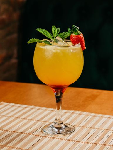 A glass containing a beverage with a strawberry garnish, resting on a colorful placemat