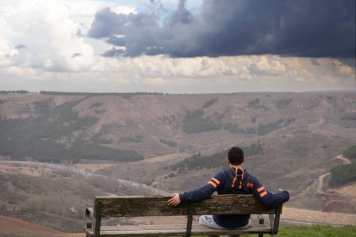 Young man sitting alone on a bench overlooking the mountain and valley. Thinking about life. Spending time alone and thinking about nature.
