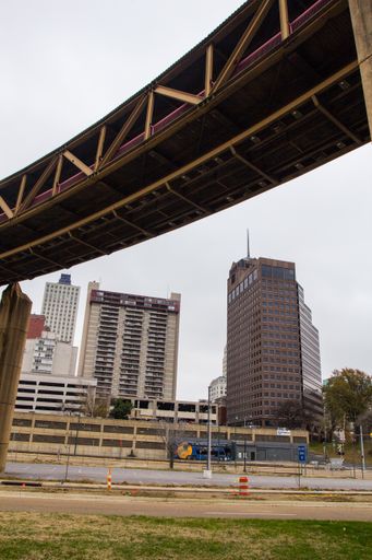 A vertical shot of a pedestrian bridge over a road with high buildings in the background