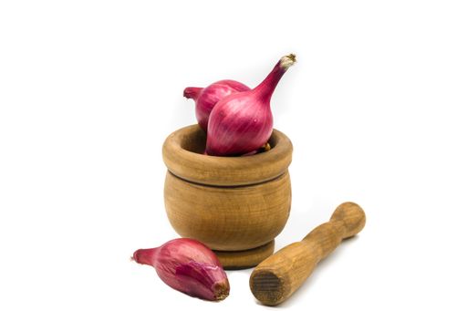 A closeup of organic red onions in an old wooden mortar isolated on a white background