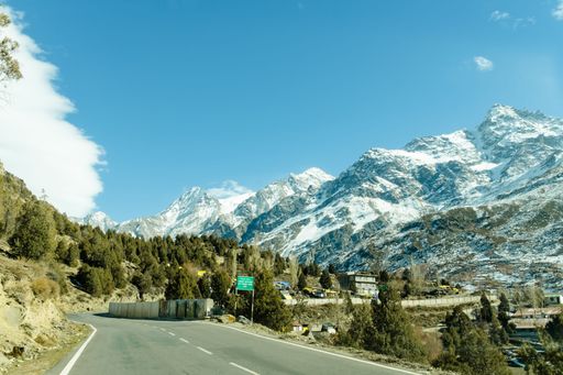 Scenic winter view from the asphalt road in the mountains covered with snow and trees on the side of the road on a background of blue sky and clouds
