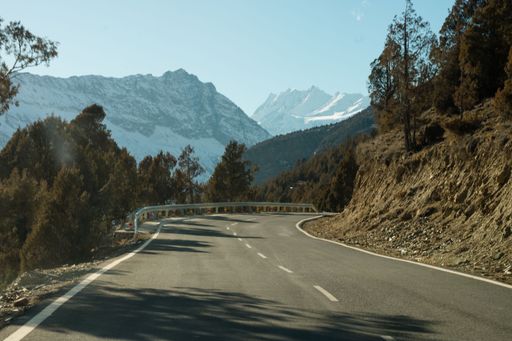 Scenic winter view from the asphalt road in the mountains covered with snow and trees on the side of the road on a background of blue sky and clouds