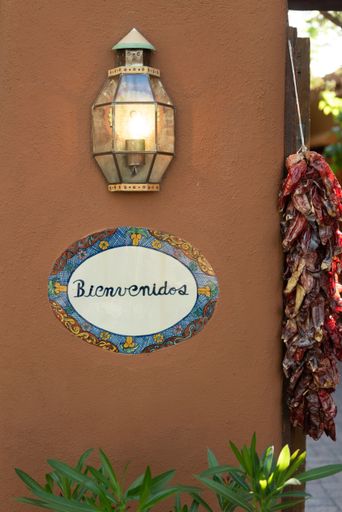 A vertical closeup a "welcome" sign in Spanish on a wall next to a lamp and dried chilies in Santa Fe