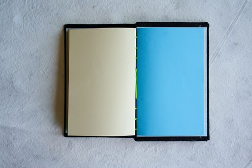 A top view of an open notebook with blank cream and light blue sheets placed on a white surface
