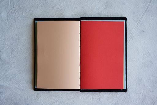 A top view of an open notebook with blank cream and red sheets placed on a white surface