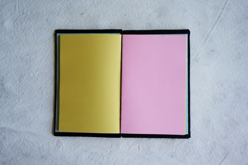 A top view of an open notebook with blank yellow and pink sheets placed on a white surface