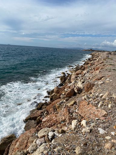 A vertical shot of a rocky coastline under a cloudy blue sky
