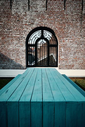 A vertical shot of a blue wooden bench in front of a building with an arch gate in Roubaix, France