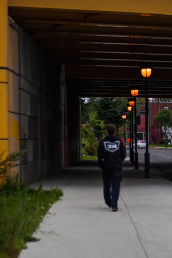 A vertical shot of a male from behind walking on the street toward the illuminated street lights