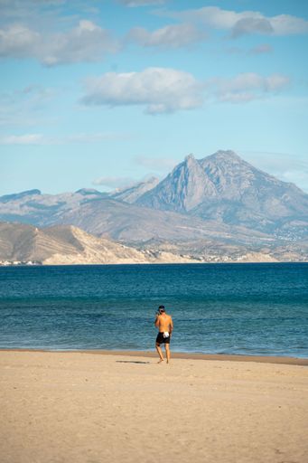 A man standing on a beach in a scenic landscape, with the majestic mountains in the background