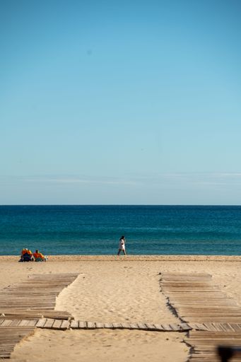 A picturesque wooden boardwalk winding its way down to the sandy shoreline, populated with people enjoying a leisurely walk on the beach