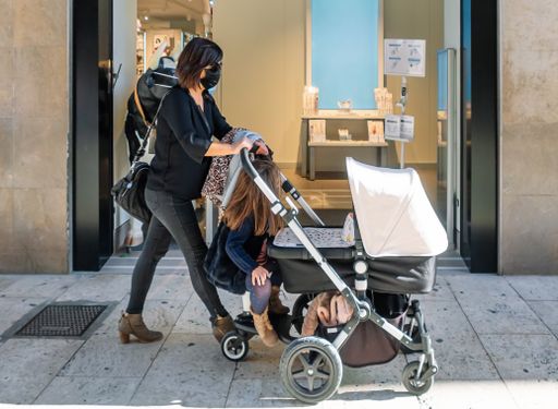 A female and her daughter with facemasks walking around the city with a baby carriage