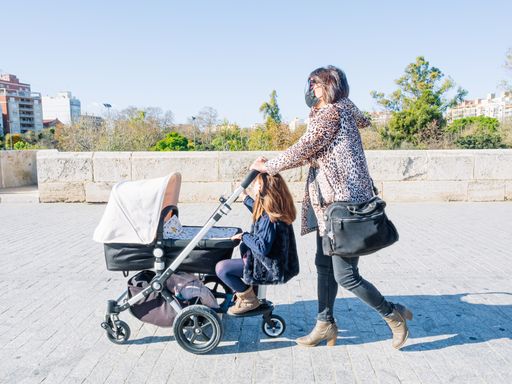 A Female and her daughter with facemasks walking around the city with a baby carriage