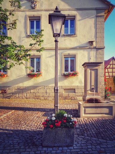 A vertical shot of an old streetlight in front of a building with windows decorated with beautiful flowers