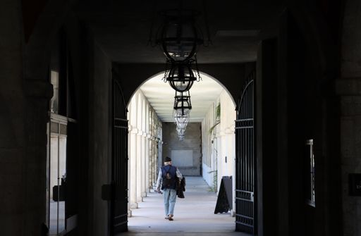 A young man wearing a grey shirt and blue jeans walking down a long hallway in an old building