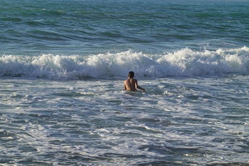 A rear view of a young man swimming on the sea with waves splashing