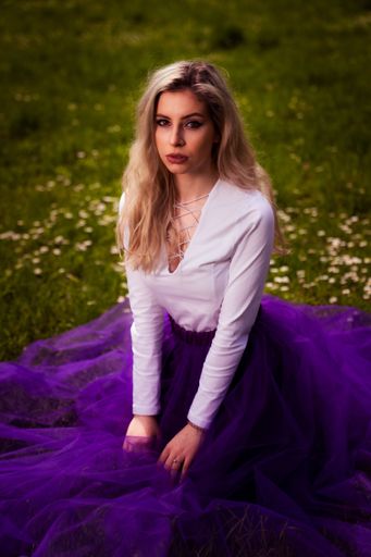 A young female posing in a white shirt and a purple tulle skirt sitting in a park