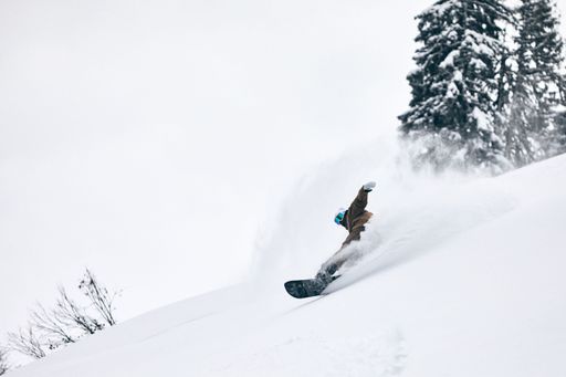 A man in a snowsport outfit performing an action turn while snowboarding down a mountain slope
