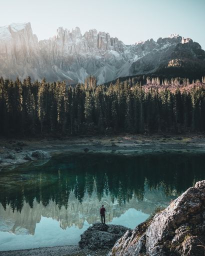 A person standing on a rock by the lake surrounded by trees and rocky mountains in Switzerland