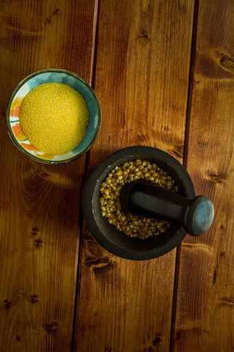 A top view of mortar and pestle with corn kernels in it on a wooden table